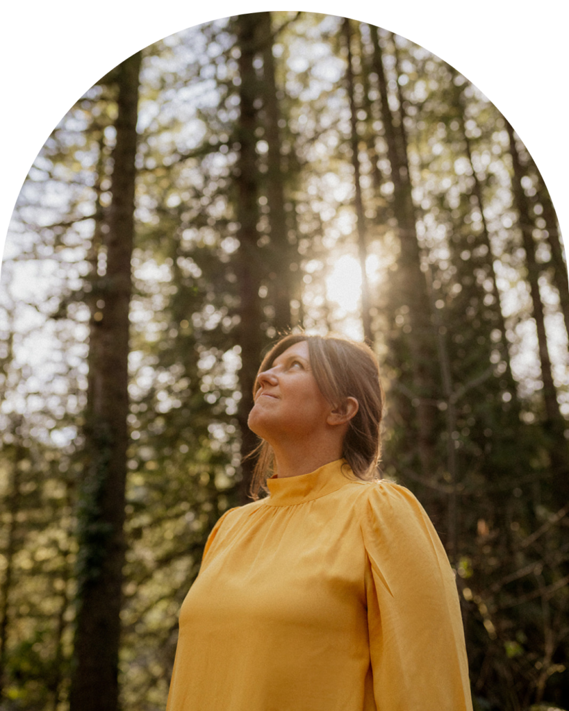 Dr. Jessica Thomas, therapist, in bright yellow top standing in nature looking at the trees